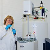Frau im weißen Kittel und mit Schutzbrille arbeitet an einem Forschungsgroßgerät.