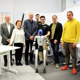 Eine Personengruppe steht mit einem Roboter in einem Labor. 